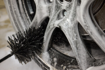 Cleaning car wheel thoroughly with brush and soap for maintenance and shiny result