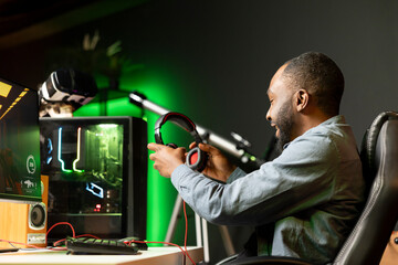 African american man putting headphones on while playing videogames at home to better immerse...