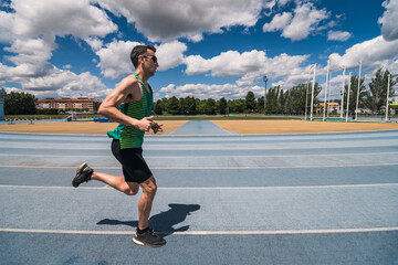 A man with sunglasses runs on a track with a green and black shirt