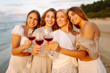 Happy young women drinking wine at summer day at the beach. Vacation, travel, sea, friendship and people concept. 