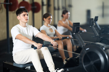 Young athletic guy in sportswear training on rowing machine in gym