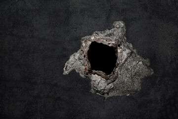 big hole in grey cement concrete wall surface texture, conceptual dark background, close up image. gap in black color painted fence. surface with big cracks and crumbling plaster. empty Copy space.