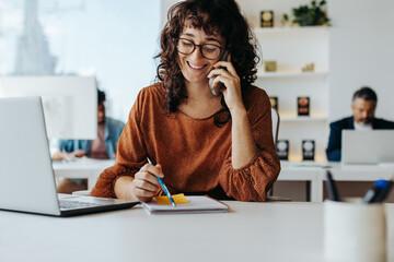 Happy businesswoman smiling and speaking on the phone at her office desk