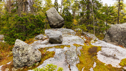 A large rock is located on an incline within a forested region