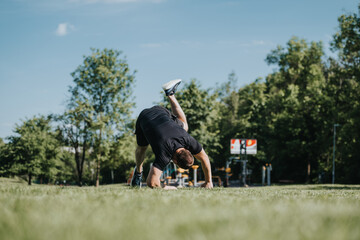 Obraz premium Man practicing a shoulder roll exercise in a park on a sunny day, demonstrating outdoor fitness and flexibility training.