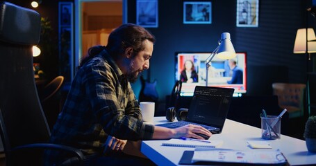 Skilled computer scientist writes code on laptop screen while in living room office using...