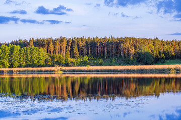 Beautiful view of a landscape with the reflection of the opposite shore in the calm waters of the lake, featuring forest trees against the backdrop of a sunset. Sweden.
