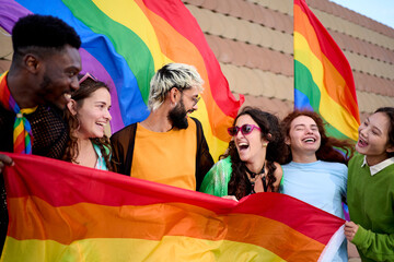 Group of excited young friends enjoying together on gay pride day. Joyful people gathered from LGBT community hugging laughing outdoors. Generation z and open minded. 