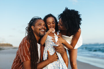 Happy family moment at the beach with mother, father, and daughter blowing bubbles