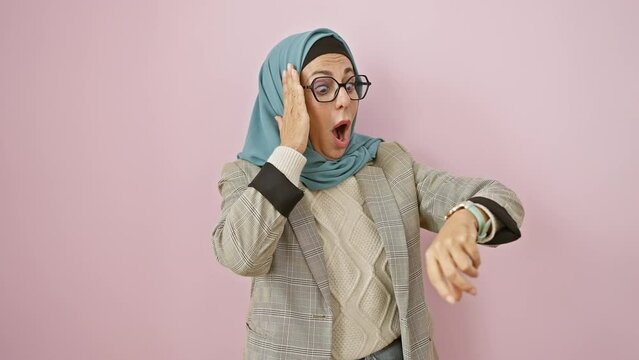 Worried middle age hispanic woman checking wristwatch, fearing late for work. in hijab, over a pink isolated background, rush against time ticks