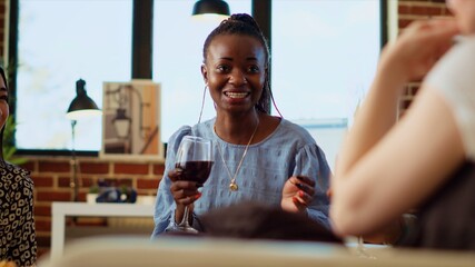 African american woman discussing with diverse apartment party guests about her boyfriend, making them laugh with hilarious tales. Happy group of people listening to host talking about partner - Powered by Adobe