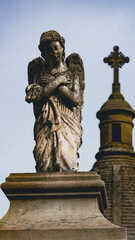 Escultura antigua de un angel arrodillado con una capilla detrás 