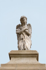 Escultura en marmol de un ángel arrodillado orando con el cielo de fondo