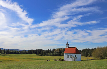 Eine kleine Kapelle im Frühlinge unter einem weiß-blauen Himmel im Allgäu
