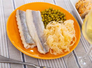 Light salted herring with pickled cabbage and green peas dished up in a plate on the laid table