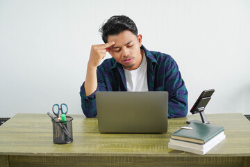 Frustrated young Asian businessman sitting at workplace because of piled up tasks