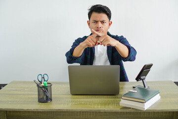 young asian businessman sitting at workplace doing gesture of rejection