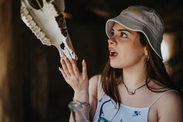 Curious young female traveler examines a horse skull in a rustic setting, showcasing her interest in local discoveries.