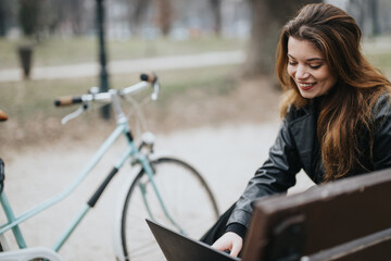 Elegant and confident young woman using a laptop outdoors, casual business setting with bike, embodying a modern, active lifestyle.