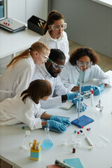 Obraz premium Vertical high angle view of young African American teacher and group of middle school students doing experiments during Chemistry class