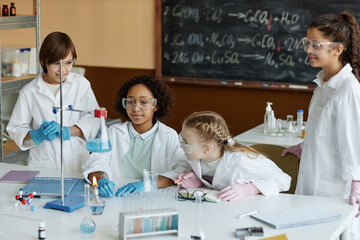 High angle view of ethnically diverse boys and girls wearing lab coats and goggles doing experiment...