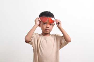 Image of Asian child posing cutely wearing red glasses on white background. portrait of an Asian boy