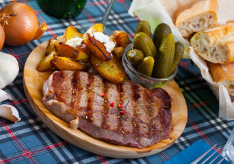 Spicy medium rare roasted veal steak with fried potato wedges with sauce and pickles on wooden board