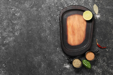 Wooden cutting board, lime and spices on dark textured table, flat lay. Space for text