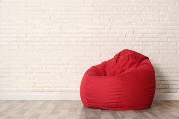 Red bean bag chair near white brick wall in room. Space for text
