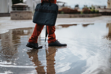 Close-up of businessperson with briefcase walking through a puddle reflecting city buildings after...