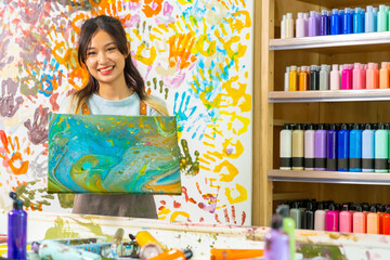 Portrait Asian generation z woman learning acrylic pouring art on canvas workshop at art studio. Young artist university student enjoy and fun creating colorful abstract modern art painting in class.
