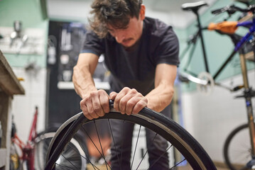Hispanic bicycle repairman mounting an airless solid tire on a bike wheel at his repair shop....