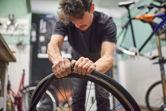 Hispanic bicycle repairman mounting an airless solid tire on a bike wheel at his repair shop. Selective focus composition with copy space. - Powered by Adobe