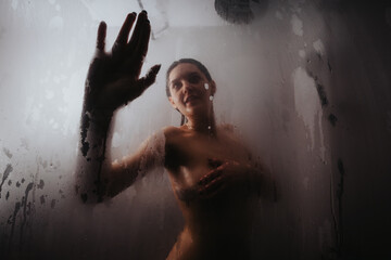 Moody and evocative portrait of a woman captured through a steamy shower glass, creating an...