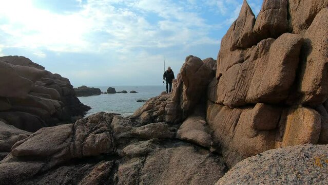 Un p&ecirc;cheur qui marche dans les rochers sur la c&ocirc;te de granit rose en Bretagne - France - 4K