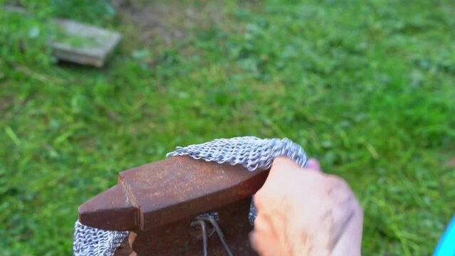 The hand of a blacksmith forges medieval chain mail from metal rings on an anvil, striking the iron with hammer. Ancient hand craft, restoration of history, reconstruction of battles, costumes, armor