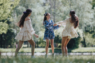 Three young women dance joyously in a lush park on a sunny day, embodying freedom and carefree...