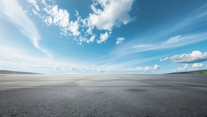 A wide shot of an empty asphalt floor with blue sky and clouds in the background.