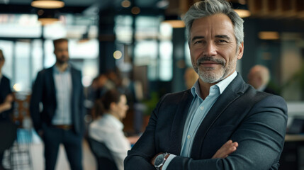 Fototapeta premium A confident businessman standing in the foreground, his arms crossed and smiling at the camera, his team standing behind him in an office setting.