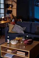 Vertical no people shot of beer bottles and snacks on wooden coffee table in living room interior, copy space