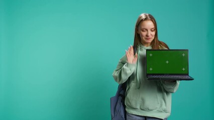 Smiling woman presenting laptop with green screen display, isolated over blue studio background. Cheerful person creating promotion with chroma key notebook device, camera B