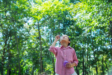 Adorable happy cute girl playful foam bubbles in green playground in summer outdoors. Funny Cheerful girl in the park with happy times.