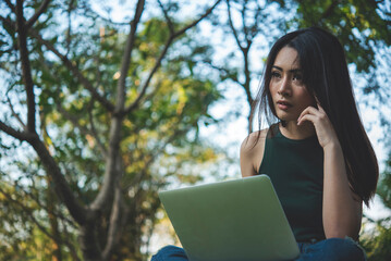 Asian woman sitting green park using laptop computer. Businesswoman failures crisis laid off...