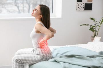 Young woman suffering from back pain in bedroom