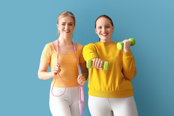 Portrait of sporty young women with skipping rope and dumbbells on blue background