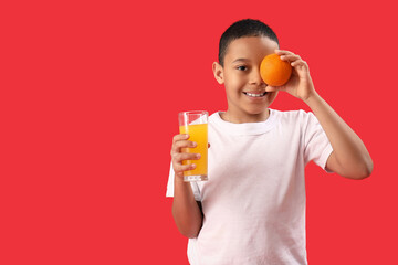 Fototapeta premium Little African-American boy with glass of juice and orange on red background