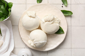 Plate of tasty Burrata cheese with basil on white tile background