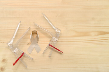 Beige ribbon with gynecological tools on light wooden background. Uterine cancer awareness concept