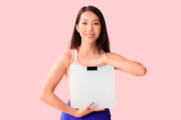 Beautiful young Asian woman with scales on pink background. Weight loss concept