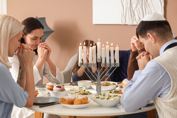 Happy Jewish family praying before dinner at home on Hanukkah